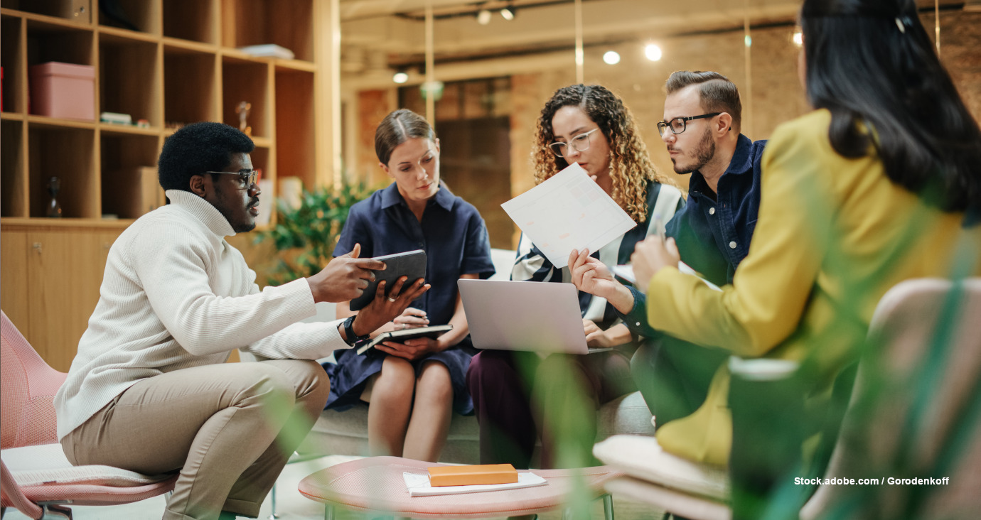 Gruppe mit 5 Personen sitzen im Büro mit Laptops und Tablets und besprechen etwas